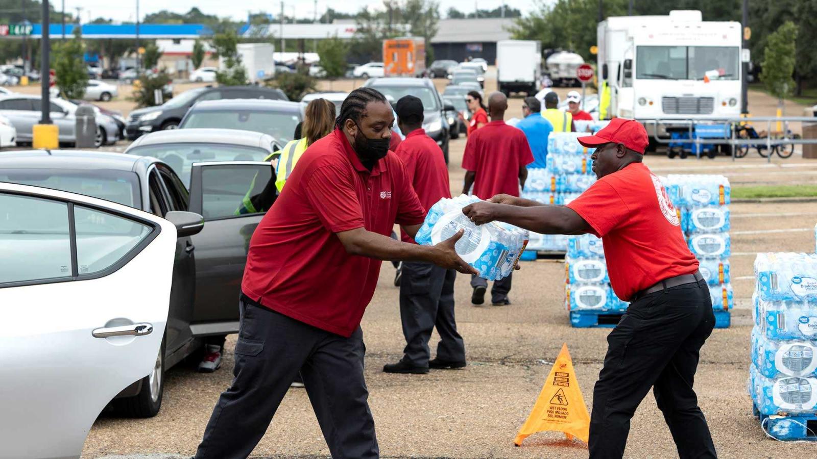 A man giving a pack of water to another man. Both are wearing red.